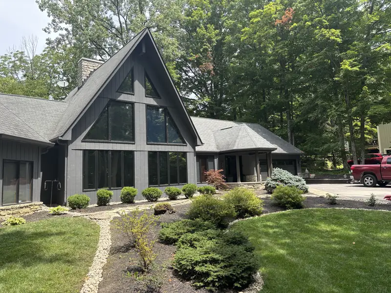 Foundation swale along the front of a gray A-frame house that turns into a river rock trench drain, running into the front yard and wrapping around the mulch bed