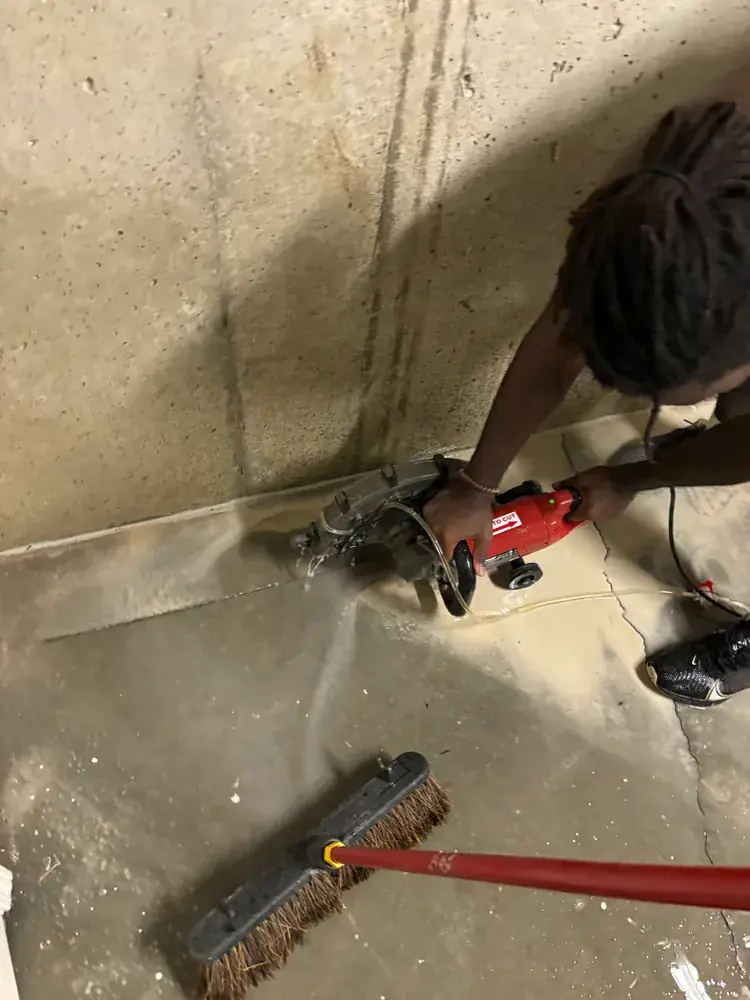 Crew member saw-cutting the concrete basement floor along the wall