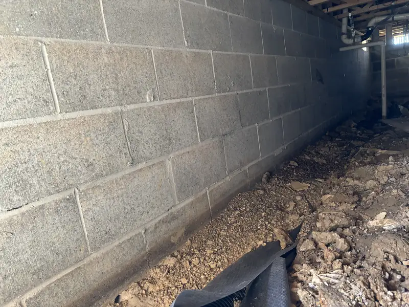 Block basement wall with the floor edge dug out and black drain material in place