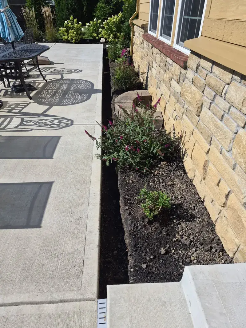 Before: a narrow trench dug by hand along a concrete patio, running to an existing concrete drain