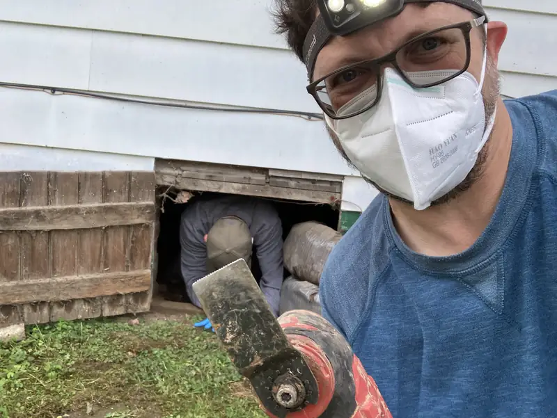 Technician in a mask at a crawlspace access opening