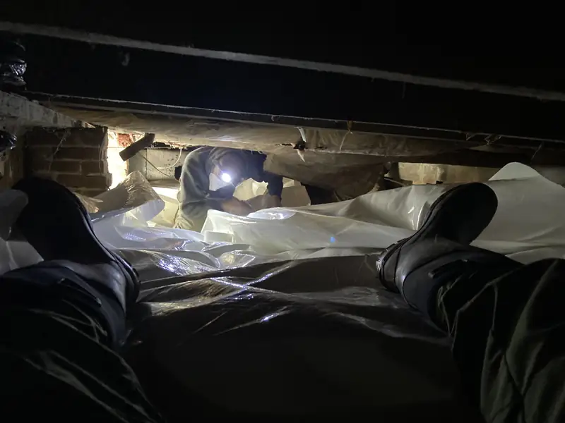 Crew laying white vapor barrier in a dark crawlspace