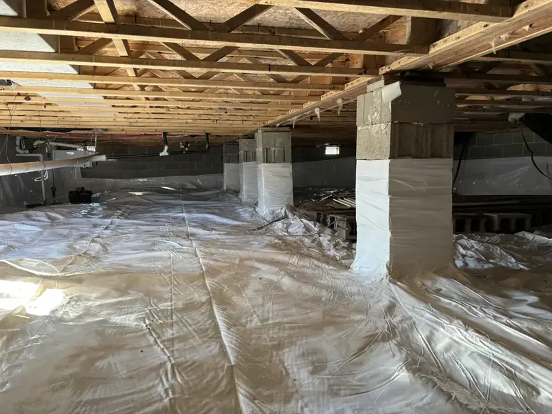 Completed crawlspace with a vapor barrier laid edge to edge across the floor and wrapped up the piers