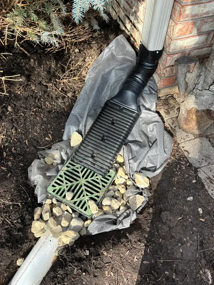 Downspout connected to a green drain grate set in stone and fabric
