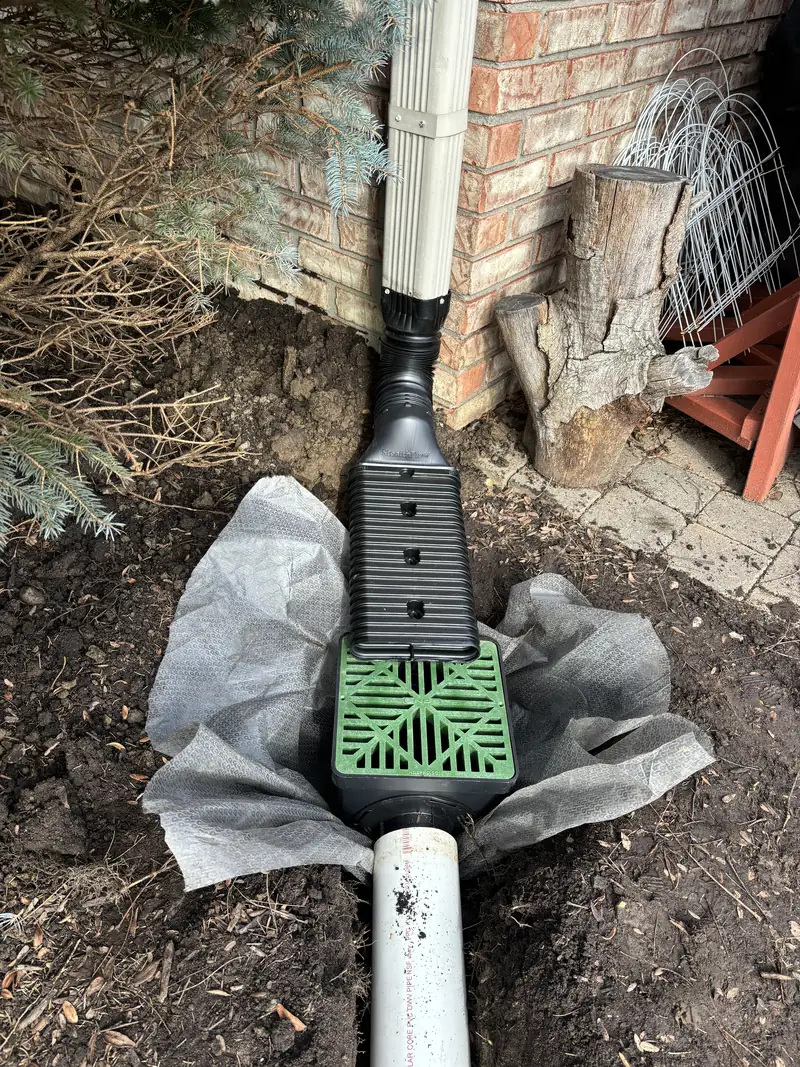 Downspout tied into a grated basin at the base of a brick wall