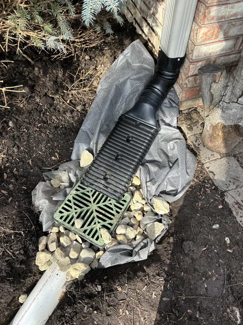 Second downspout tied into a grated basin at a brick wall