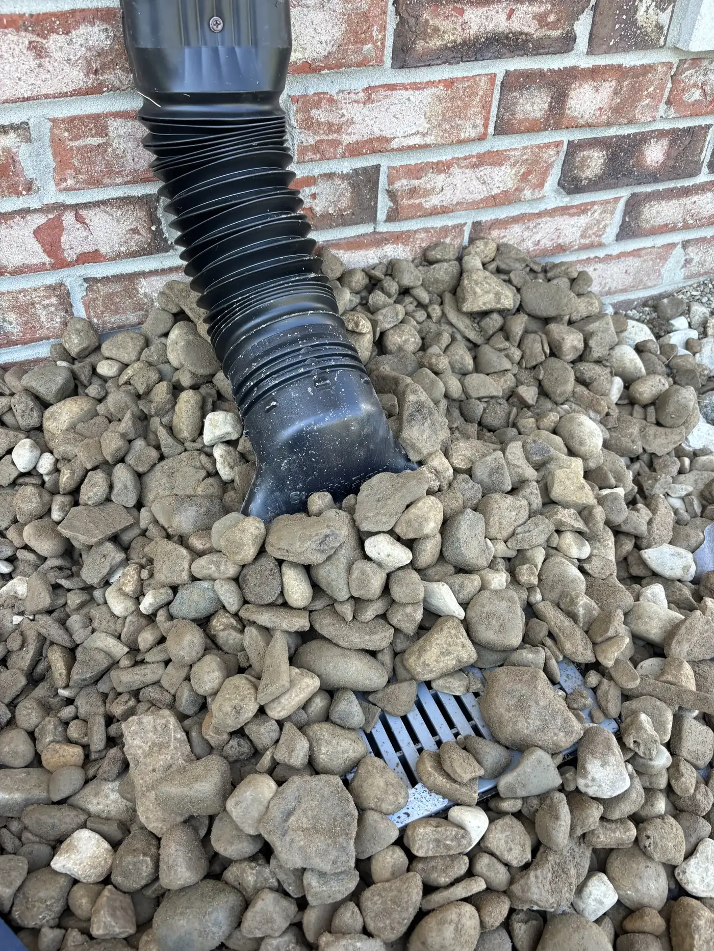 Downspout with a flexible black adapter running into a rock bed