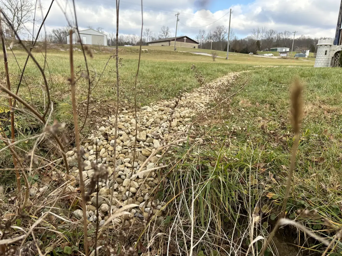 A hand-dug drainage line running across an open Howard County lawn toward a low spot in the field beyond