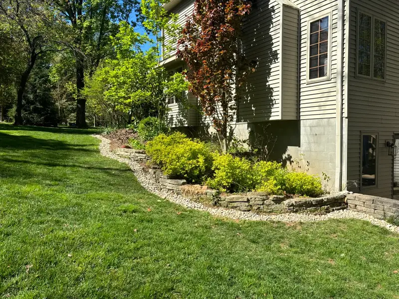 Finished side yard with stone edging, a white rock strip against the foundation, new shrubs and full green grass