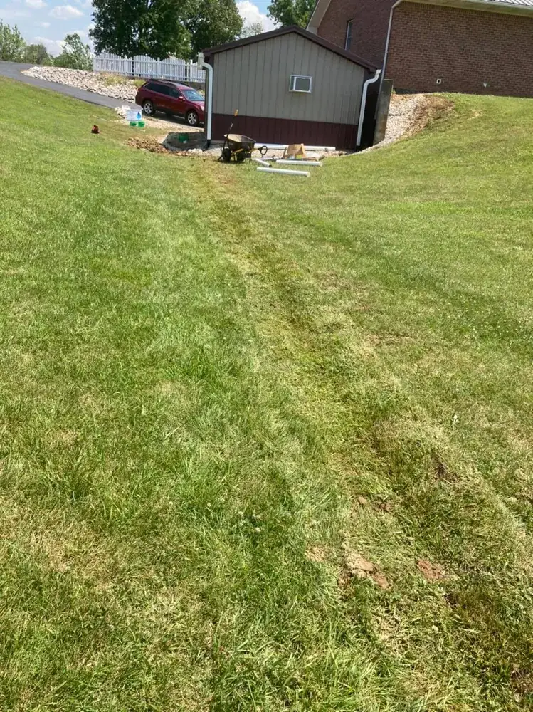 A finished grass swale carrying water across a mowed lawn away from a house, with the turf fully grown back over the line