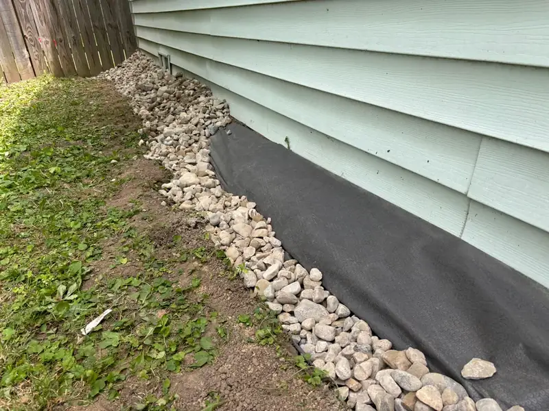 Narrow stone strip laid over black fabric against the siding of a house