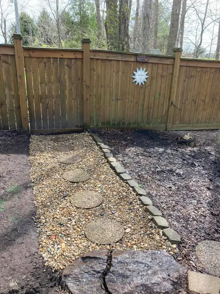 Stepping-stone path set in gravel along a wood fence, with a trench drain hidden underneath