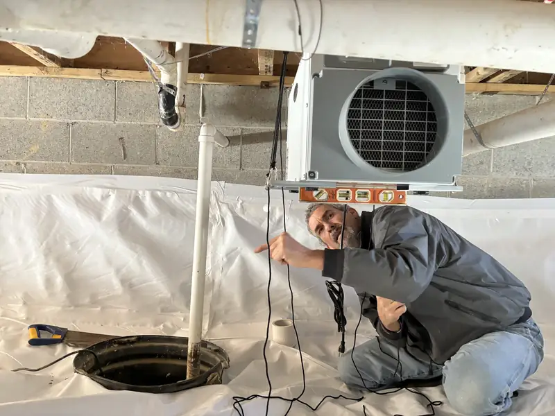 Technician kneeling beside a sump pit on white vapor barrier