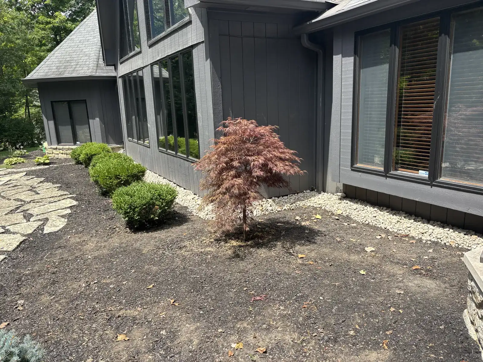 River rock foundation swale along the front of a gray house, with the glass entry door in view