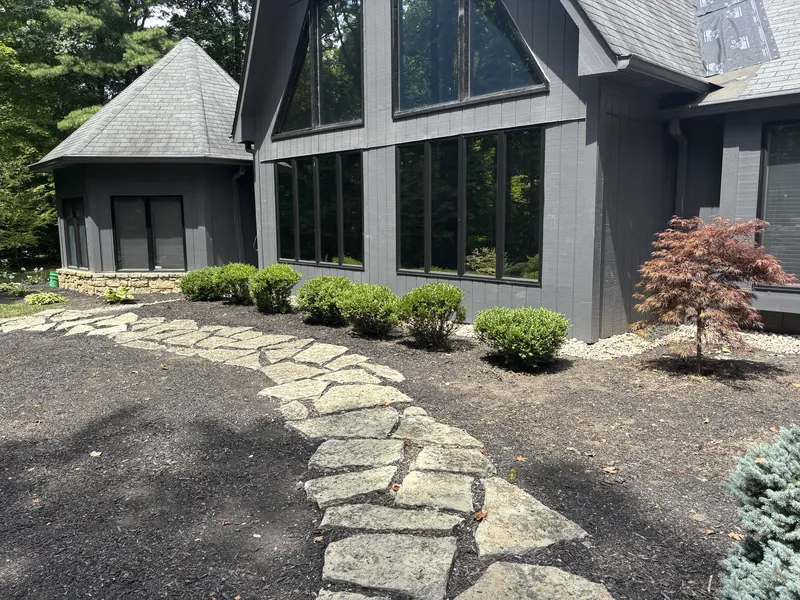 River rock foundation swale along the front of a gray house, beside a flagstone path