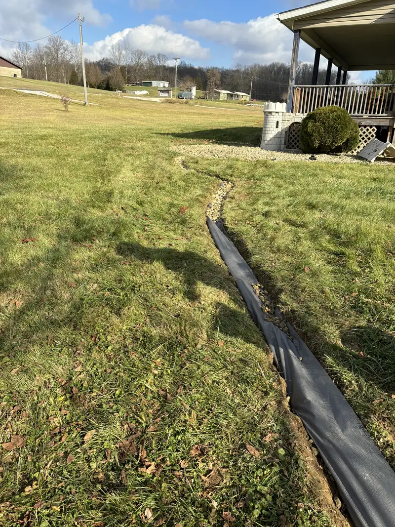 Fabric-lined trench cut across a lawn toward a house with a covered porch