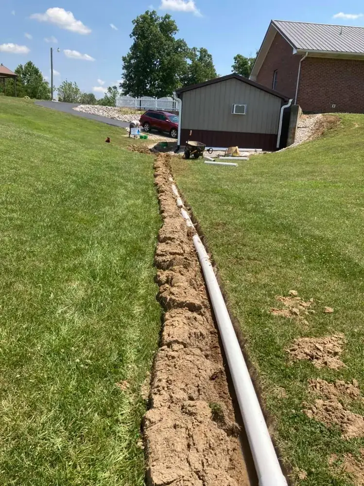 Long open trench with white solid pipe running toward a house